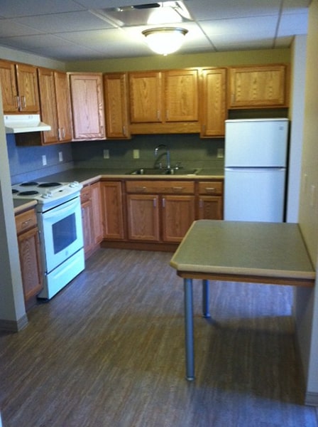 Margaret Wagner Apartments kitchen with light wood cabinets, white appliances, and small table