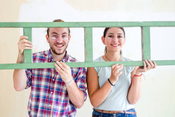 Two homeowners posing with a ladder. Their cheeks are smeared with white paint.