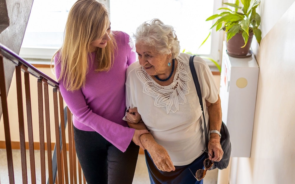 A caregiver helping her older loved one walk up the stairs