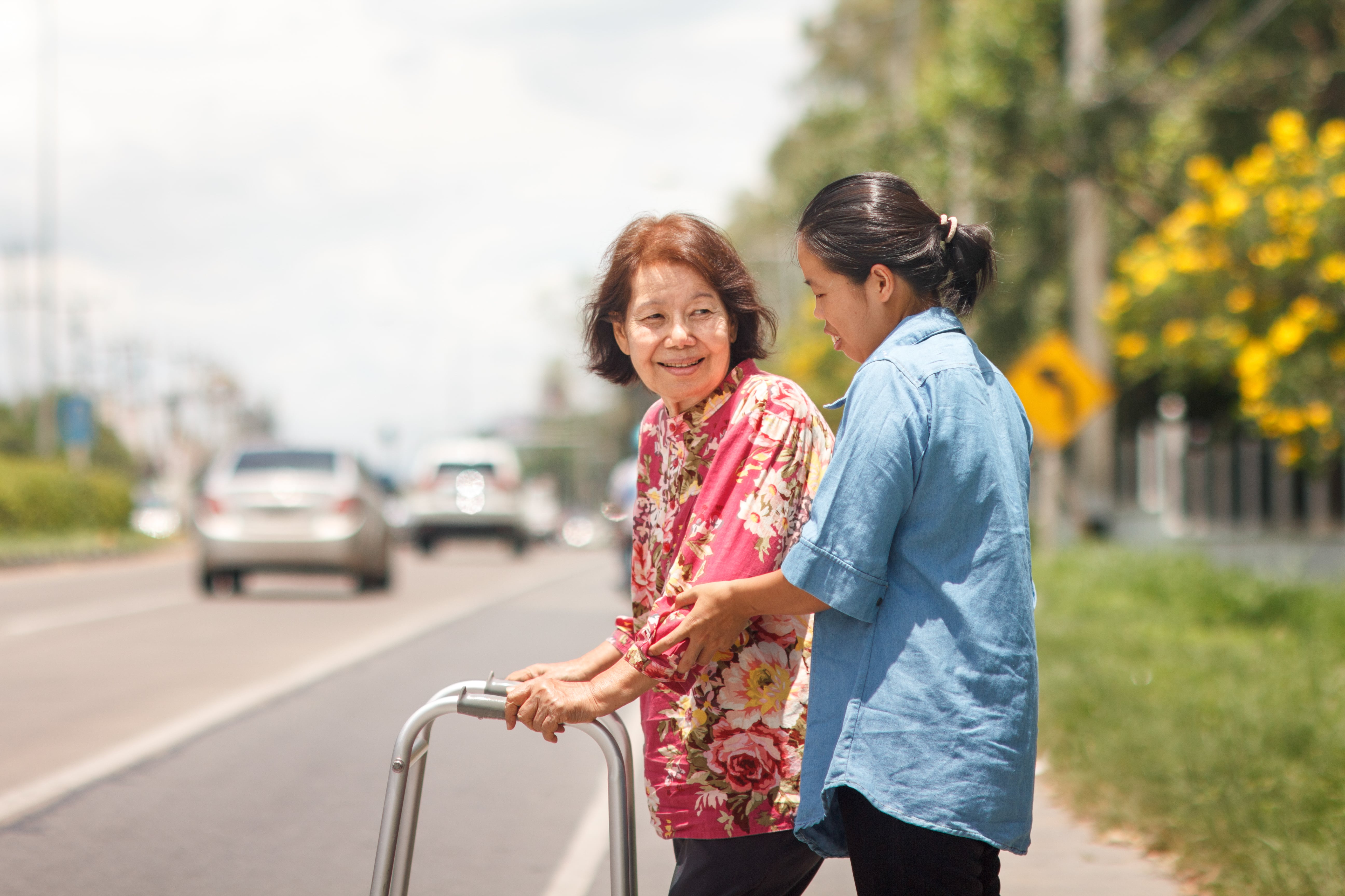 A caregiver helping a loved one with a walker walk down the street