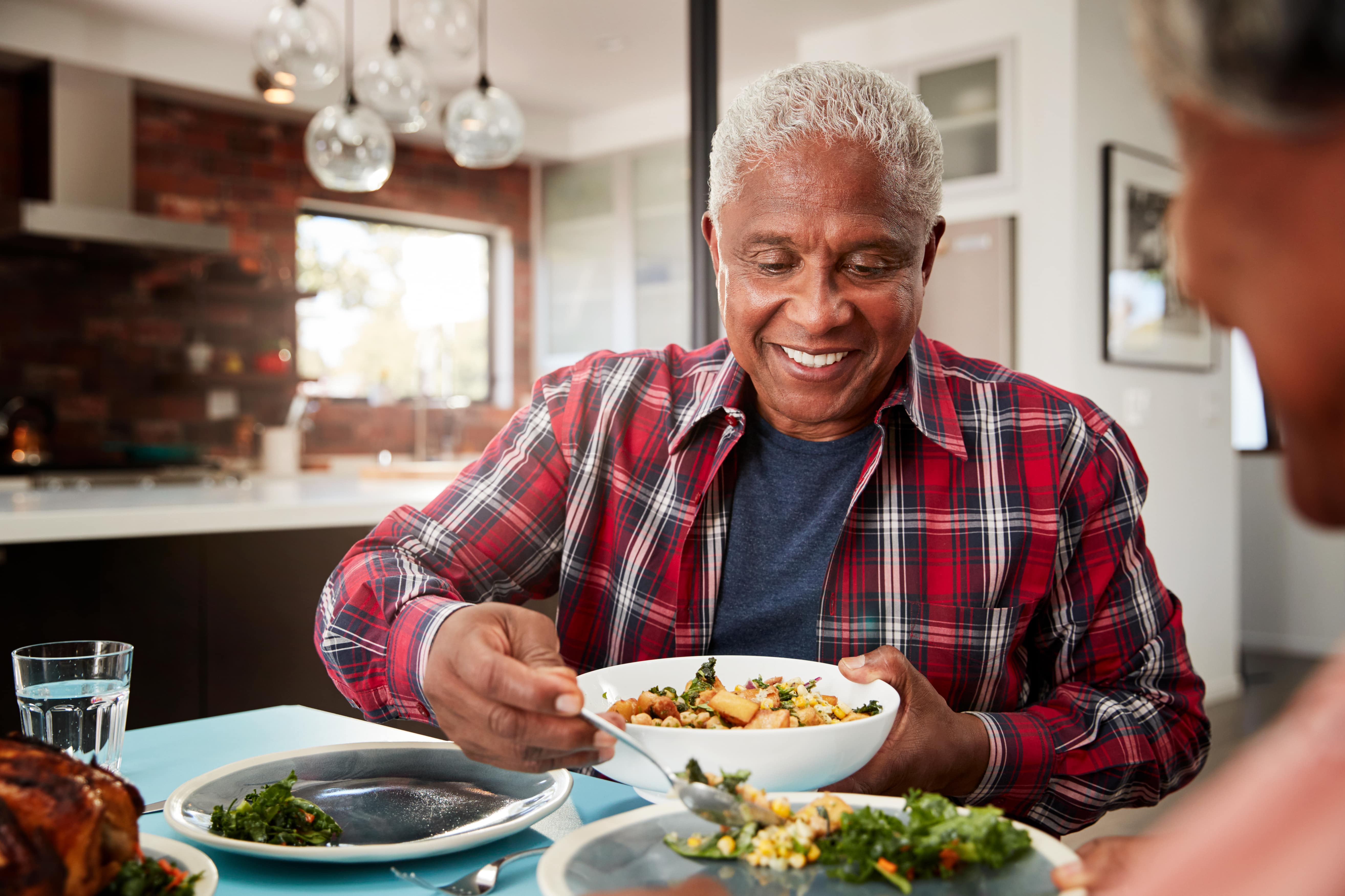 An older adult filling a family member's plate with a healthy salad 
