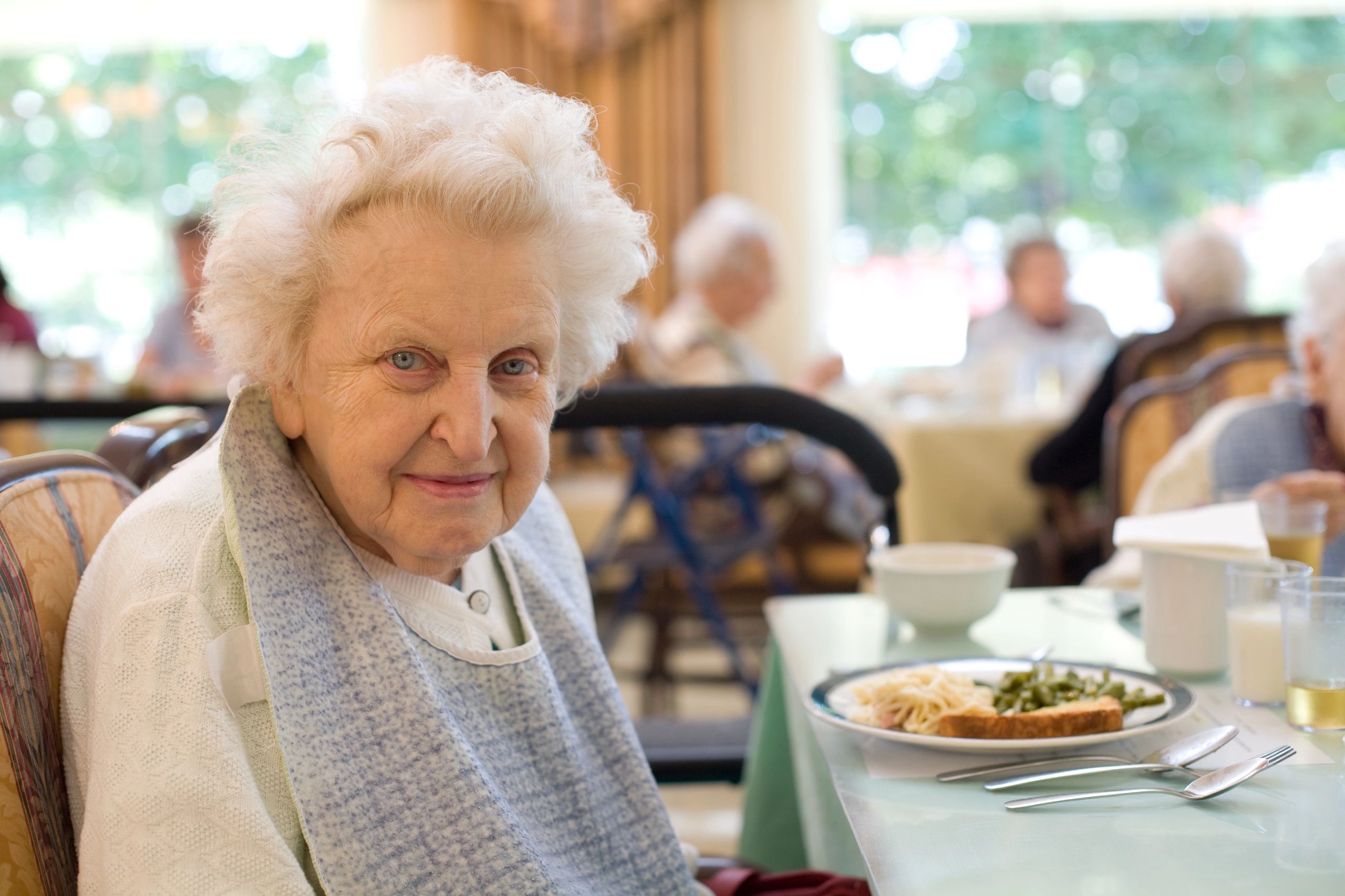 An older adult seated with her plate at a dinner table 