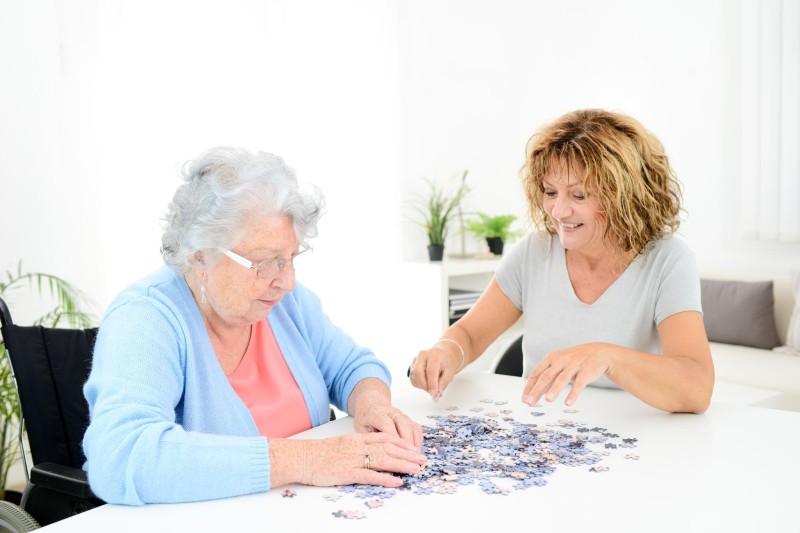 An older adult and their caregiver working on a jigsaw puzzle